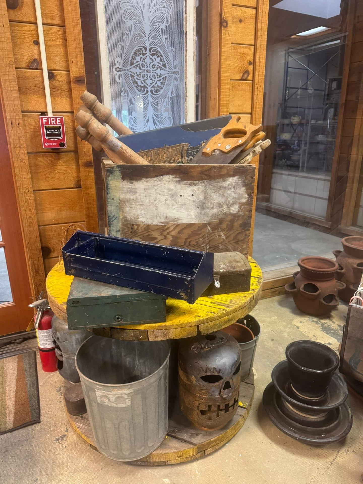 A crate of vintage hand saws, toolboxes, and rusty oddities on a wooden spool.