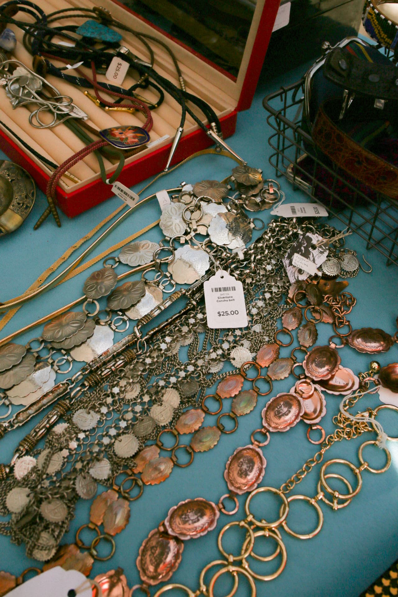 Vintage silver and copper concho belts, bolo ties, and jewelry laid out on a vendor table.