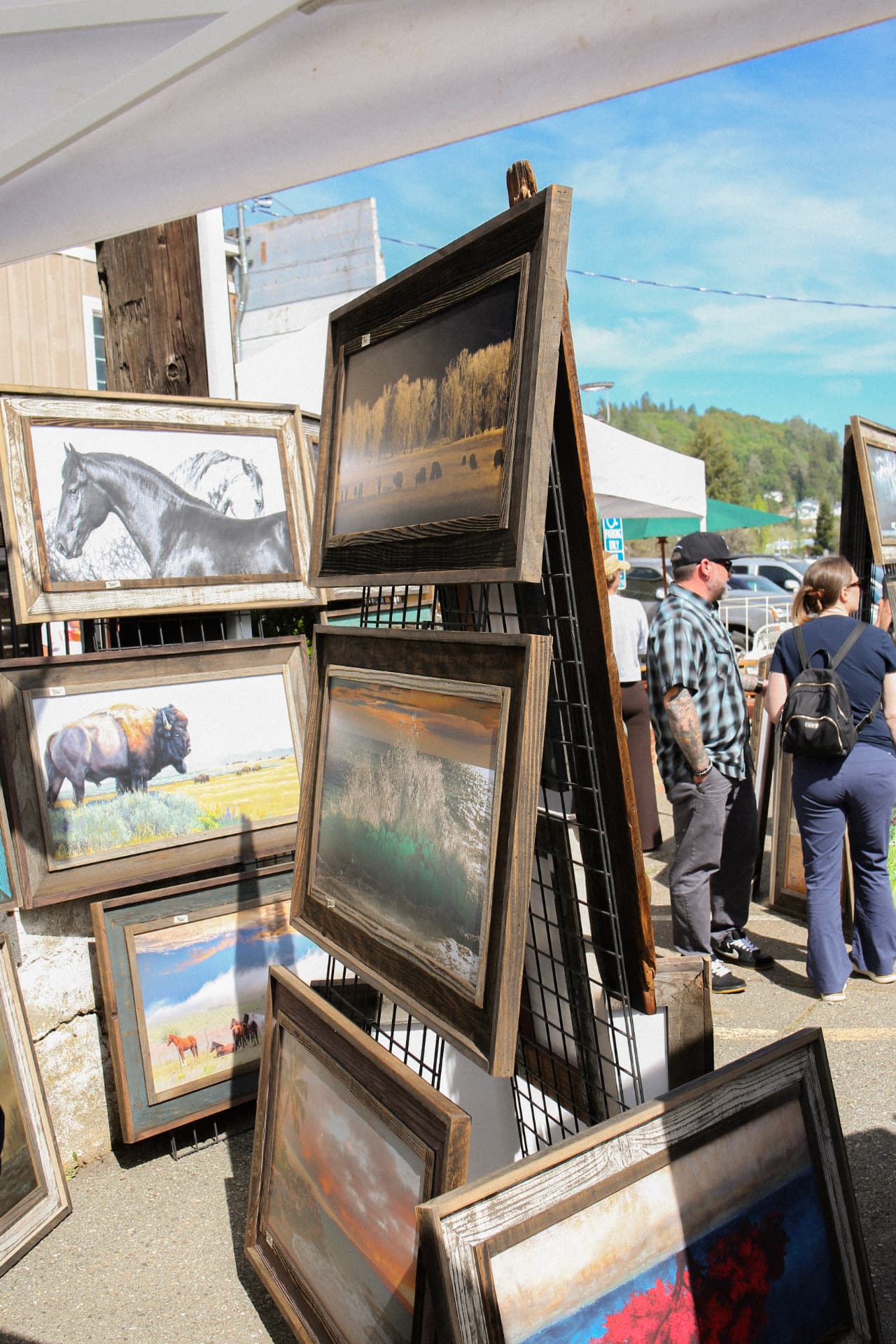 Framed western landscape and wildlife art displayed on a rack at the Bazaar.