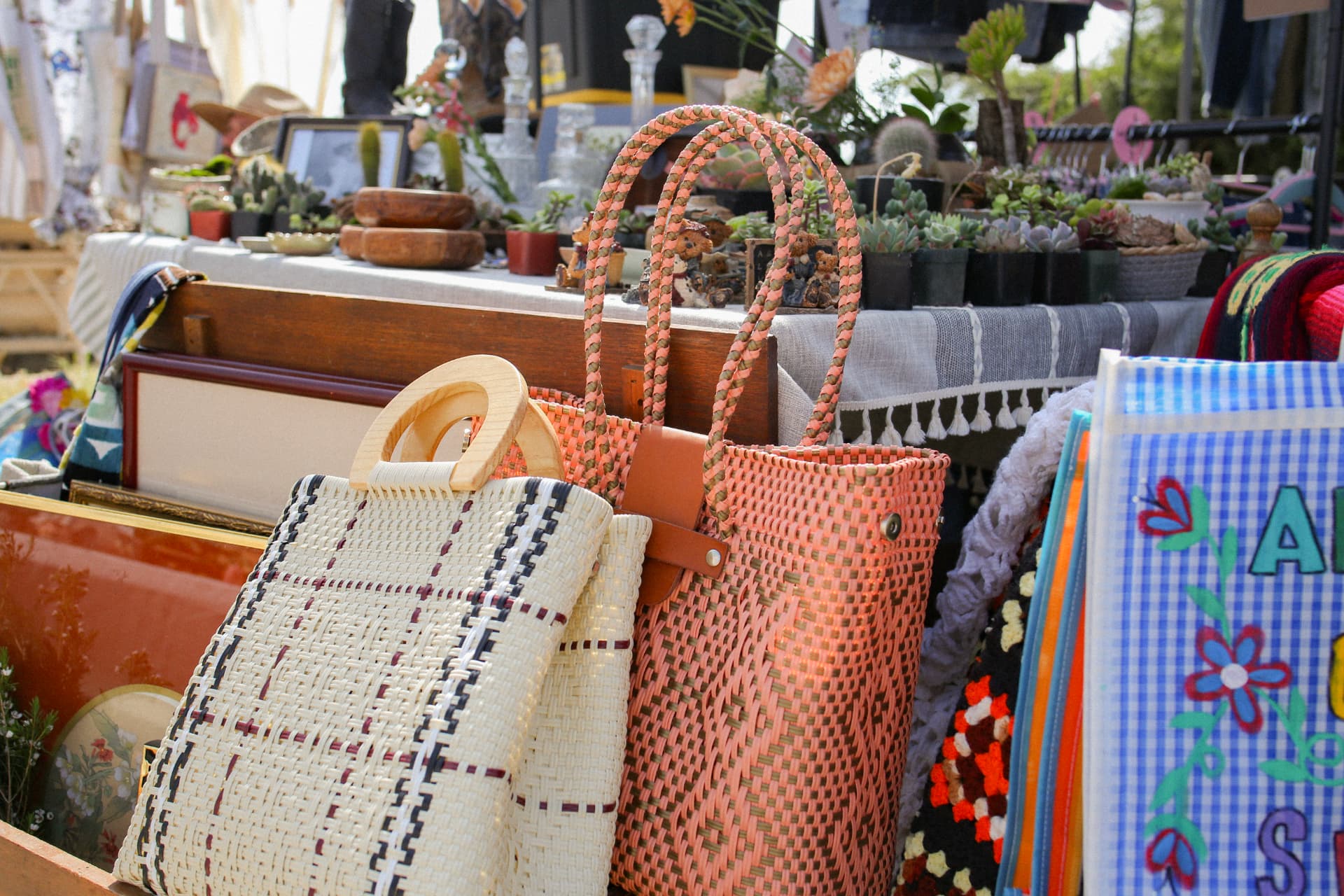 Handwoven tote bags in coral and cream displayed among vintage frames and succulents.