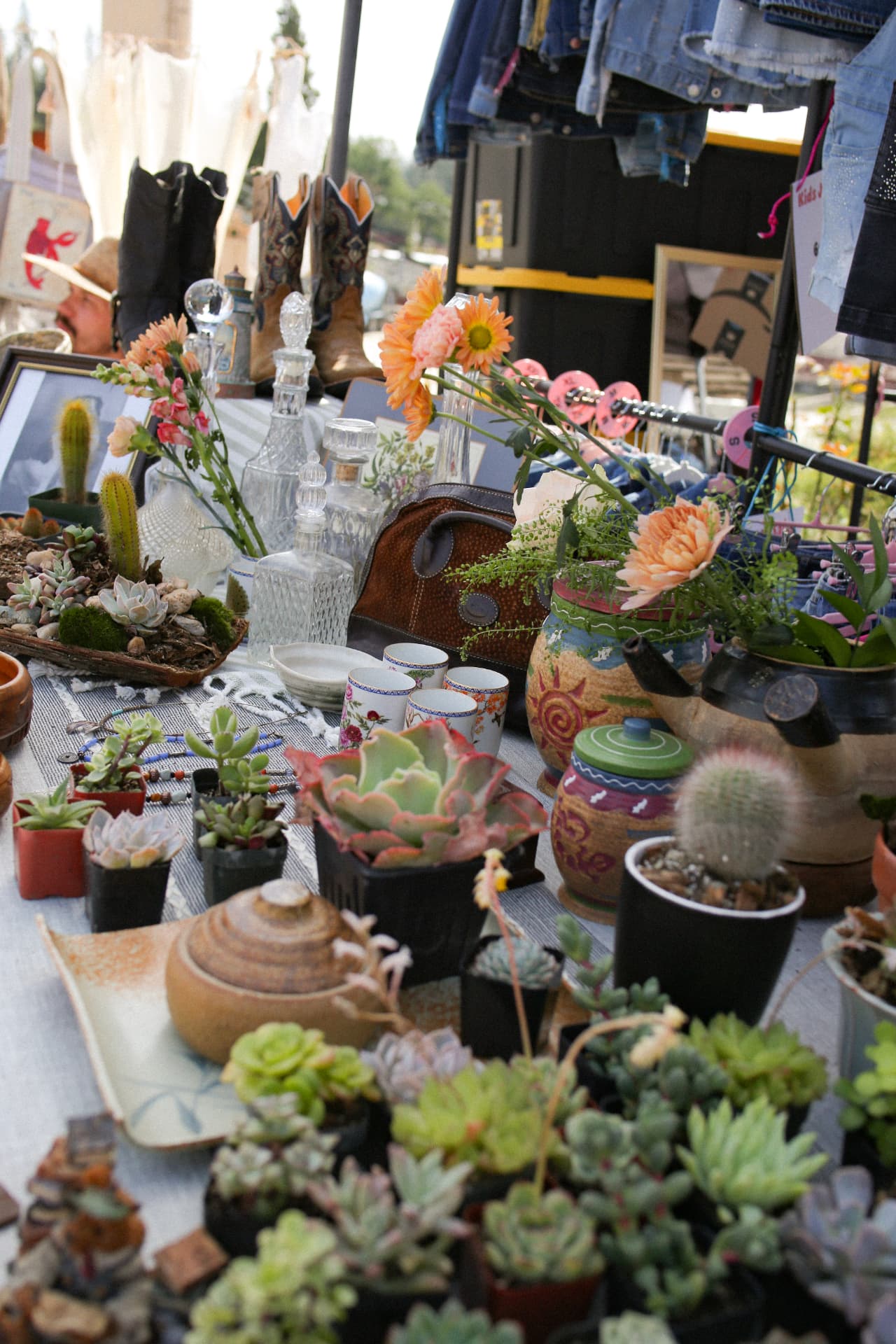 A vendor table packed with succulents, cut flowers, antique glass bottles, and cowboy boots.
